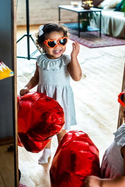 chica con piel oscura y negra, celebra el día de san valentín. Globos y vasos de lámina roja en forma de corazón.