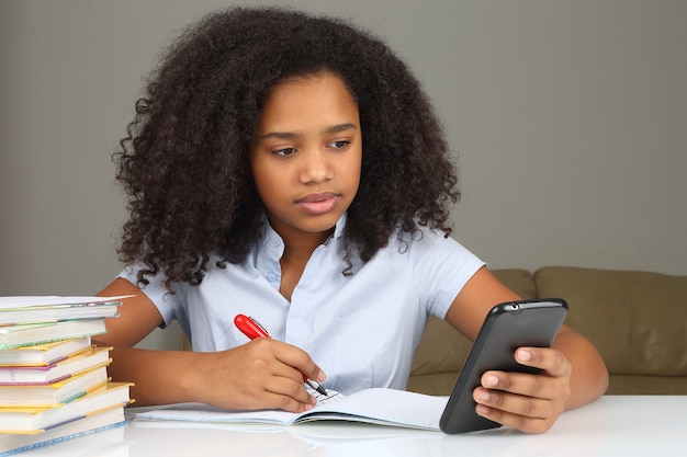 Chica de piel oscura con smartphone haciendo la tarea