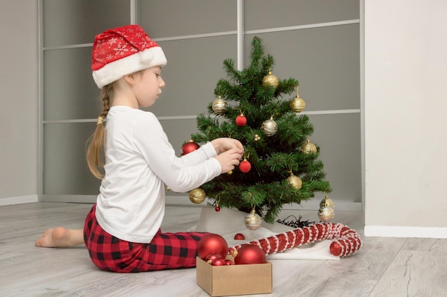 Chica en pijama y gorro de santa decora el árbol de navidad contenido navideño