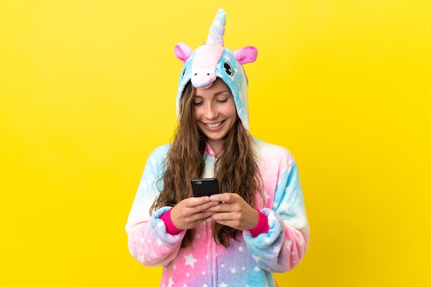 Chica con pijama de unicornio sobre un fondo aislado enviando un mensaje con el móvil