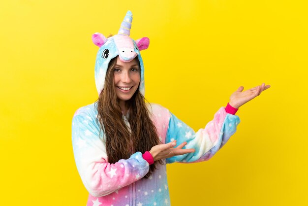 Chica con pijama de unicornio sobre fondo aislado extendiendo las manos hacia el lado para invitar a venir