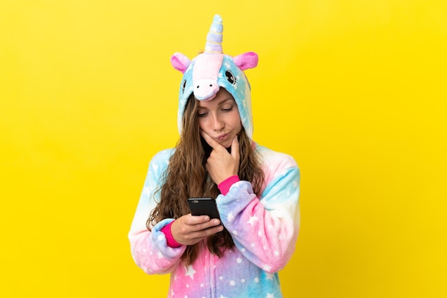 Chica con pijama de unicornio sobre fondo aislado pensando y enviando un mensaje