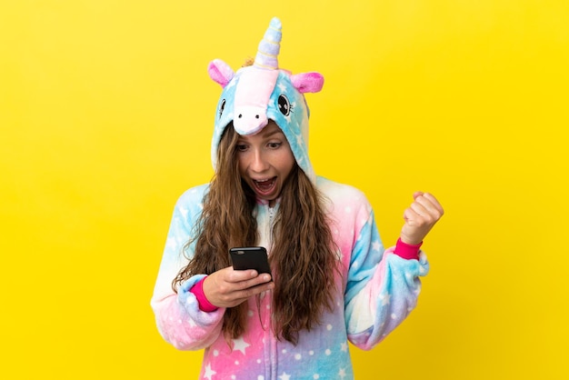 Chica con pijama de unicornio sobre un fondo aislado sorprendida y enviando un mensaje