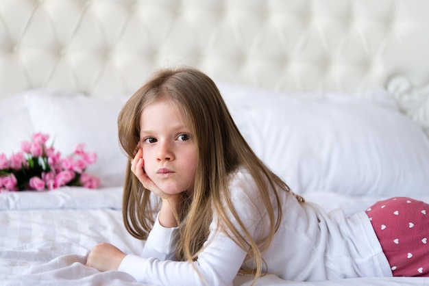 chica en pijama yace en una cama con sábanas blancas. Decoración floral.