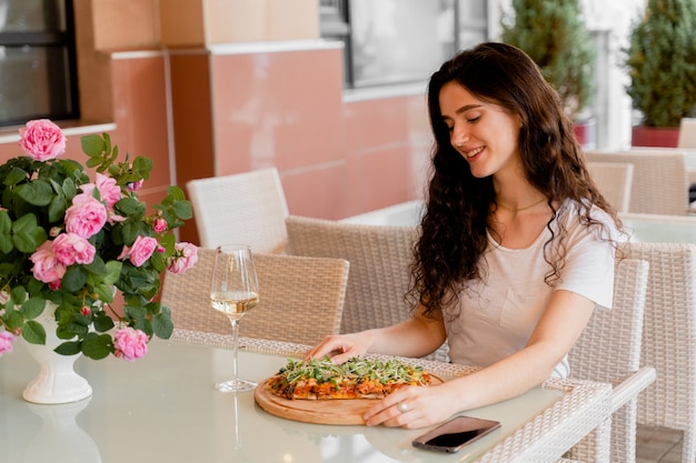 Chica con pinsa romana en café en terraza de verano. Mujer joven comiendo pinsa y bebiendo vino.