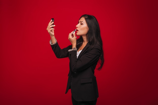 Chica pinta sus labios sobre un fondo rojo.