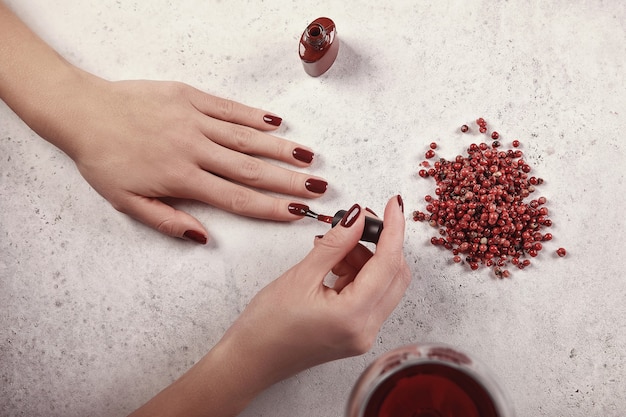 Chica se pinta las uñas con el esmalte en gel. Fondo blanco, copa de vino, detalles en rojo. Mano hermosa. Extensión de uñas. Manicura, Salón Spa. Creativo, publicitario.