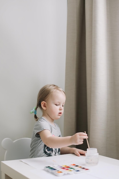 Chica pintando y dibujando con pintura de acuarela en la mesa desarrollo del potencial creativo en los niños