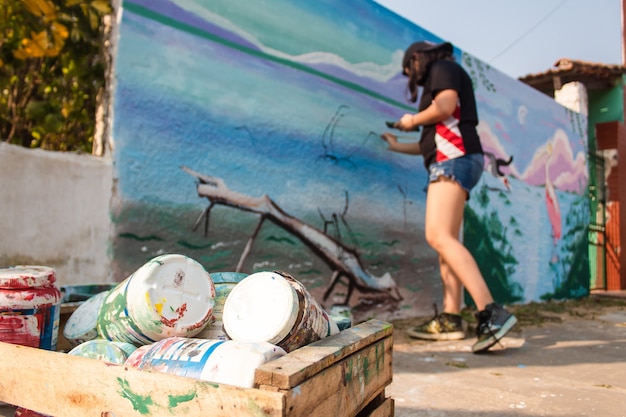 Chica pintando una pared de la calle con pinceles.