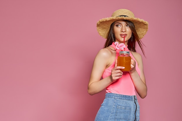Chica de playa hermosa alegre con sombrero de verano posando en traje de baño de cuerpo con cóctel en mano