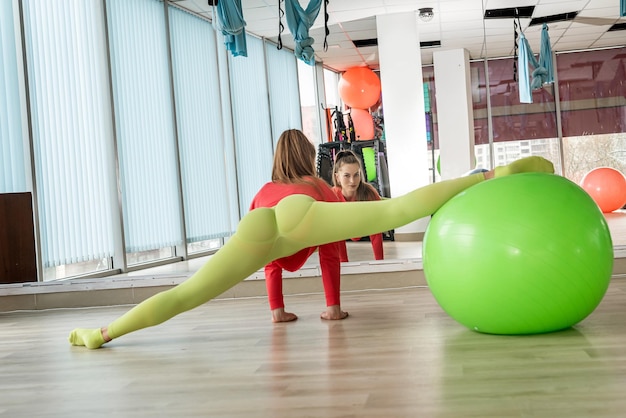 Una chica con polainas de color verde claro se estira en un gimnasio de élite frente a un espejo