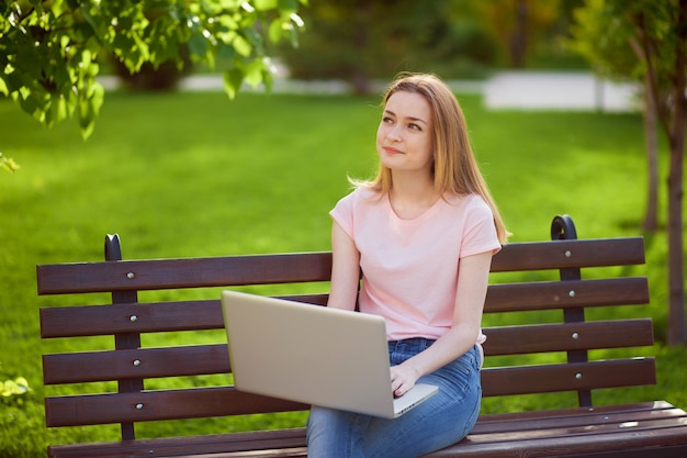 Chica con un portátil sentado en un banco en el parque