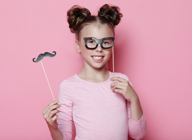 Chica posa con accesorios de fotomatón gafas y bigote Niño niña con gafas de fiesta sobre fondo rosa