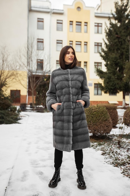 Foto chica posando en la carretera en el fondo de invierno mujer joven divertida y glamorosa con una sonrisa con un elegante abrigo de piel largo gris concepto de piel y moda gente hermosa