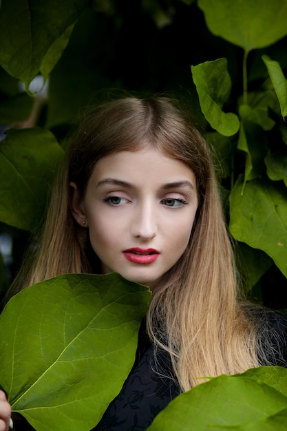 Chica posando en la pared con hojas verdes.