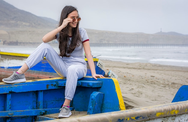 Chica posando sentada en un barco en la playa