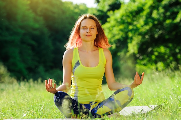 Chica posando yoga afuera en el bosque por la mañana