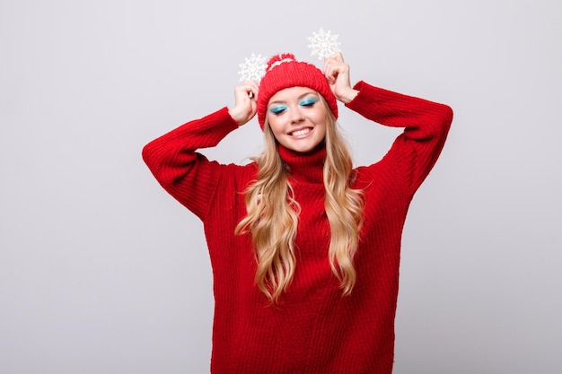 Una chica positiva en ropa de invierno con maquillaje y copos de nieve sobre un fondo gris