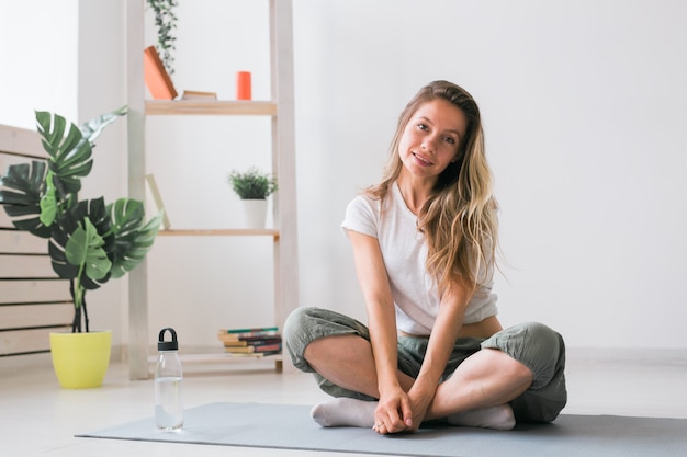 Chica positiva sentada en la estera de fitness descansando después de la práctica de pilates o yoga y atención plena