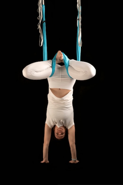 Chica practica fly yoga mujer joven boca abajo durante un ejercicio de gimnasia aérea aislado sobre fondo negro