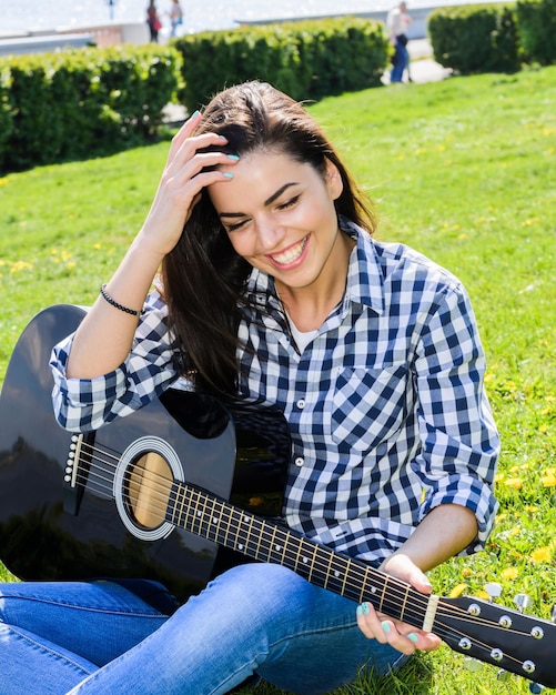 Chica en un prado verde tocando la guitarra