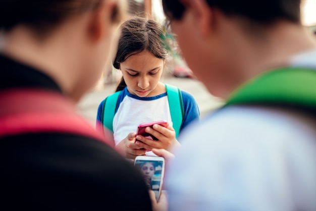 Chica preocupada de pie entre amigos y usando teléfonos inteligentes