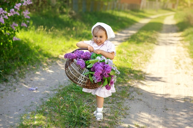 Una chica del pueblo lleva una canasta llena de flores de primavera y lilas violetas a lo largo de un camino rural