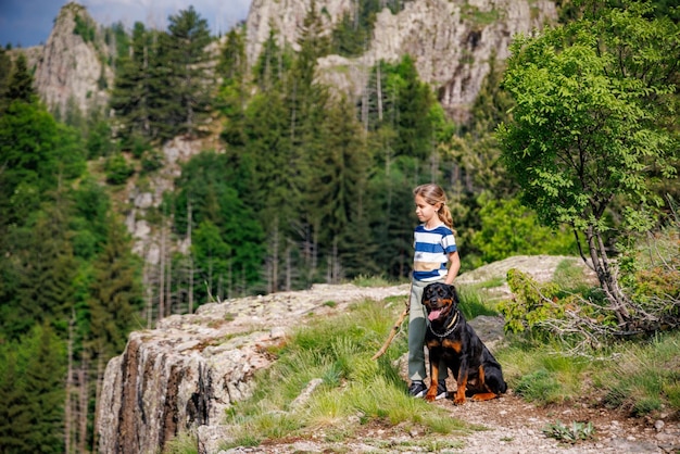 Chica con puestos junto a su perro de la raza Rottweiler en un pico con vegetación contra el cielo nublado