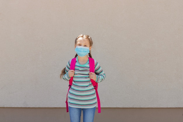 Chica que llevaba una máscara protectora con una mochila a la espalda en el patio de la escuela