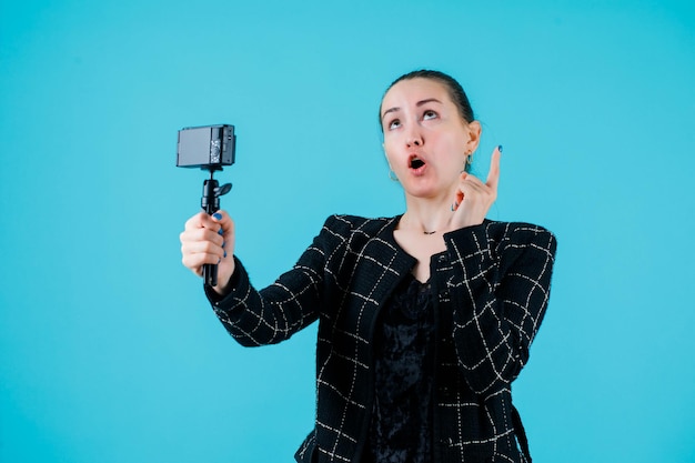 La chica que mira hacia arriba se está tomando una selfie con su cámara apuntando hacia el fondo azul