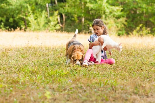 Una chica que se ríe divirtiéndose jugando al aire libre junto con su Beagle y su gato blanco