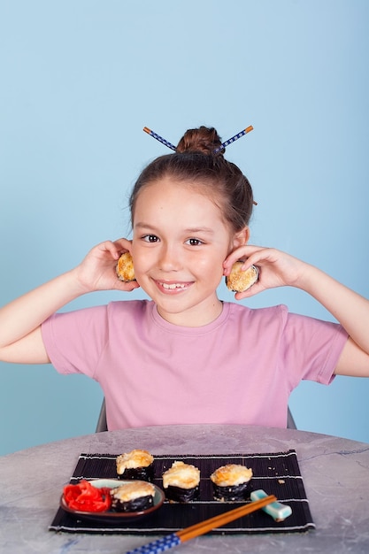 La chica que sostiene los bollos tiene una cara como binoculares Entrega a domicilio de cocina japonesa Sobre un fondo azul con un vestido rosa Cabello largo y rizado Es ridículo y estúpido