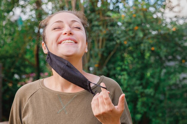 chica se quita la máscara protectora de la cara al aire libre. Mujer joven quitando la máscara después de la vacunación