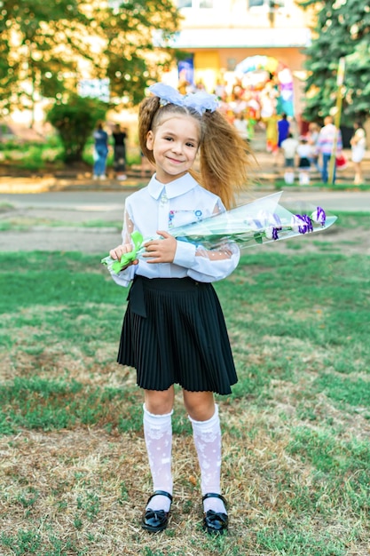 Una chica con un ramo de flores en una blusa blanca con lazos en el fondo de la escuela. Celebraciones el primero de septiembre.