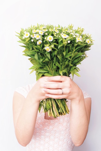 Chica con ramo de flores de margarita de campo sobre el fondo blanco.