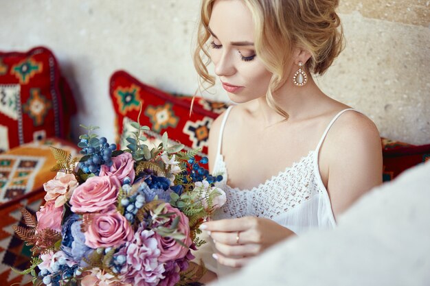 Chica con un ramo de flores en sus manos está esperando a su amado hombre cerca de la casa. peinado perfecto, cabello rizado. historia de amor