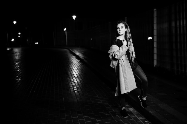 Chica con rastas caminando por la noche calle de la ciudad.