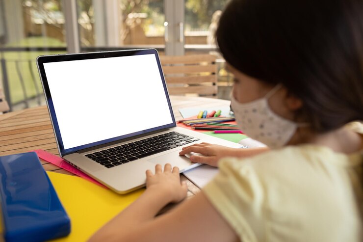 Foto chica de raza mixta pasando tiempo en casa, sentada junto a la mesa, usando una computadora portátil. distanciamiento social durante la cuarentena del coronavirus covid 19