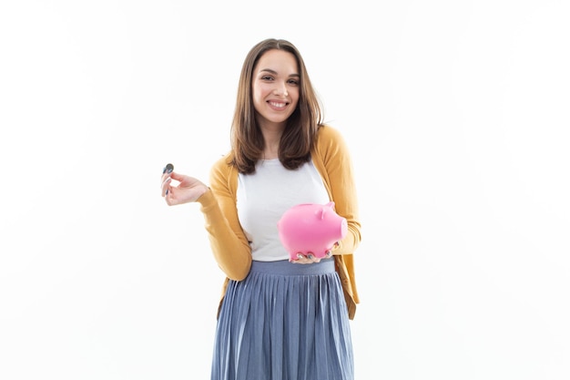 Chica recoge dinero en una alcancía rosa sobre un fondo blanco.