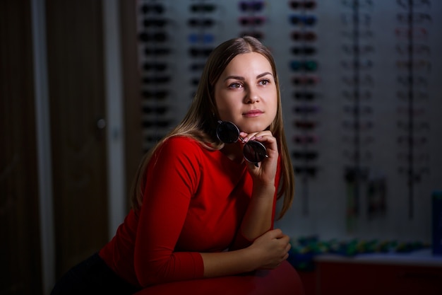 Chica recoge gafas de sol. Tienda de anteojos. Corrección de la visión. Soporte de gafas