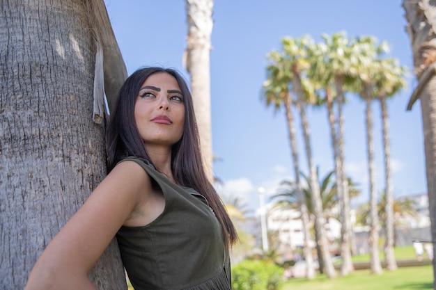 Chica se recuesta en la palmera y mira a su alrededor, está de vacaciones en Tenerife y se divierte