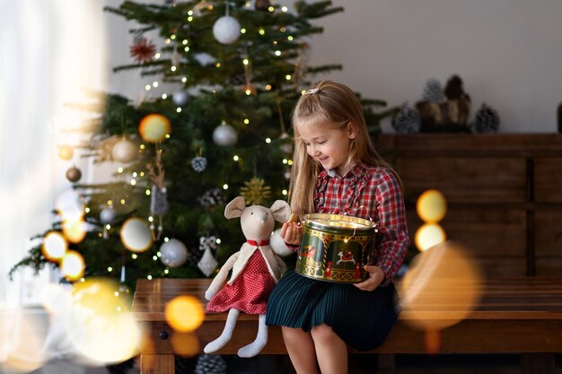 Chica con un regalo se sienta cerca del árbol de Navidad