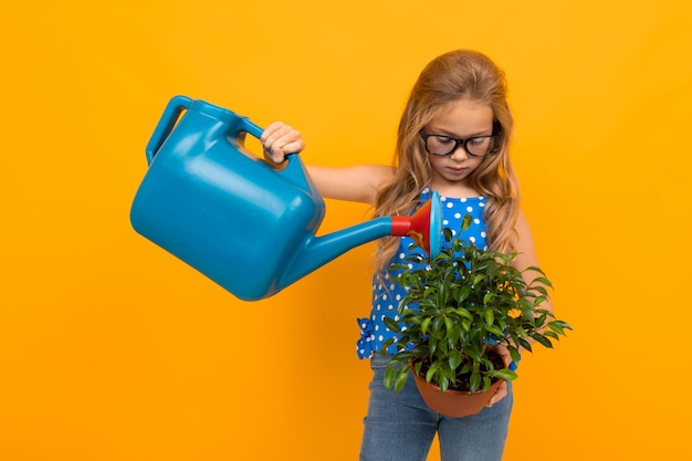 Chica regando una planta de interior en maceta en un amarillo con espacio de copia