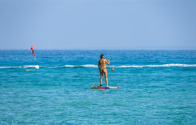 Una chica con un remo flota en una tabla en el mar