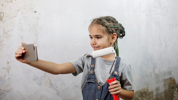 Chica reparando habitación, pintando la pared con color blanco y haciendo selfie en smartphone