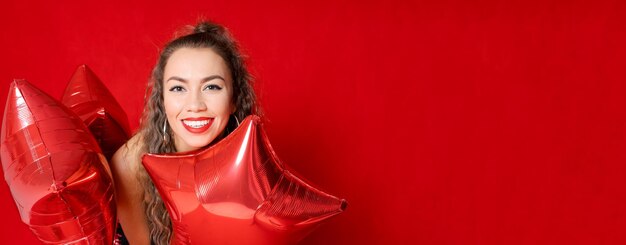 Chica de retrato de contenido sincero sosteniendo muchos globos rojos en forma de estrellas disfrutan