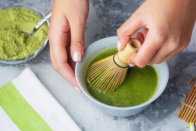 Chica revuelve té verde matcha un batidor de bambú. El proceso de hacer un primer plano de té