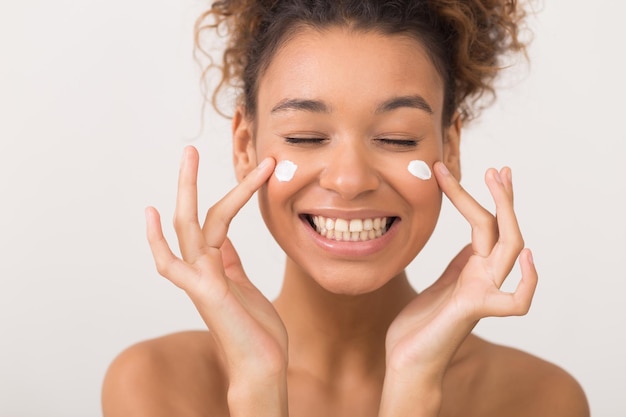 Foto chica riendo aplicando crema hidratante en la cara