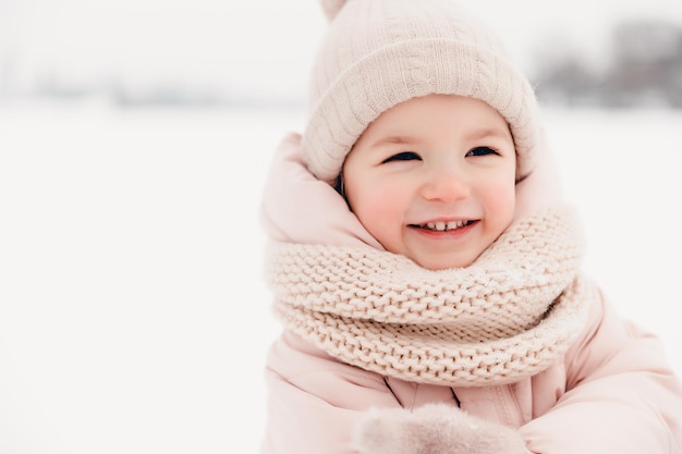 Chica riendo feliz con una bufanda de chaqueta rosa y sombrero jugando en un hermoso paseo nevado de invierno Chica disfruta de un día helado de invierno Jugando con nieve en las vacaciones de invierno Concepto de vacaciones de invierno