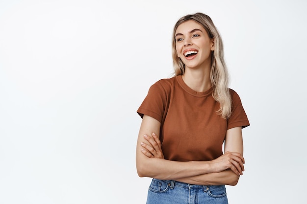 Chica riendo feliz mirando a un lado los brazos cruzados en el pecho y sonriendo mirando el logo o anuncio de pie en camiseta sobre fondo blanco.